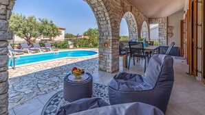 Un espace aménagé au bord de la piscine, avec des piliers en pierre, des chaises longues et une table entourée de chaises.