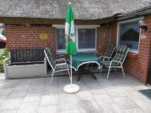 A patio with a table and chairs, a green umbrella, and a brick building with windows. - Old fisherman's house, Germany (Mönkebude)