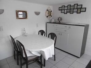 A dining area with a round table, four chairs, a white cabinet, and wall decorations including a framed picture and a welcome sign.
