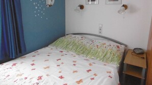A bedroom with a bed, a wall with a moon and stars design, two framed pictures, and a nightstand with a lamp. - Old fisherman's house, Germany (Mönkebude)
