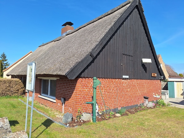 A house with a steep thatched roof, a brick facade, and a chimney.