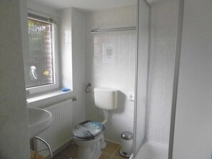 A bathroom with a toilet, a sink, a window, and a shower area. - Old fisherman's house, Germany (Mönkebude)