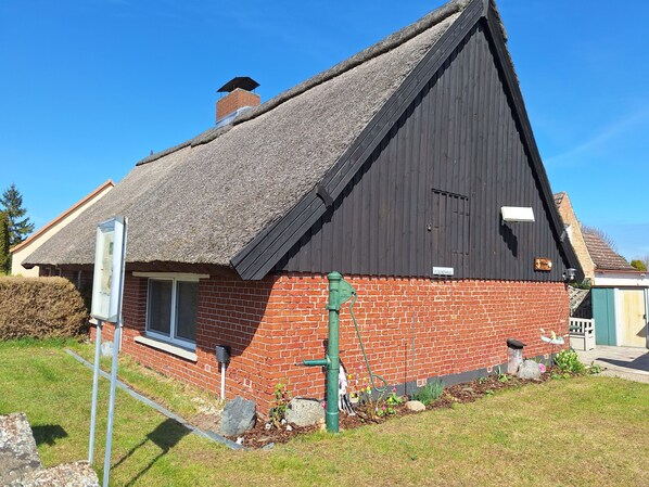 A house with a steep thatched roof, a brick facade, and a chimney.