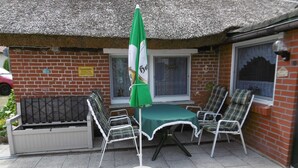 A patio with a table and chairs, a green umbrella, and a brick building with windows. - Old fisherman's house, Germany (Mönkebude)