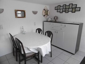 A dining area with a round table, four chairs, a white cabinet, and wall decorations including a framed picture and a welcome sign. - Old fisherman's house, Germany (Mönkebude)