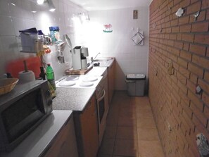 A kitchen with a microwave, stove, sink, and a trash bin.