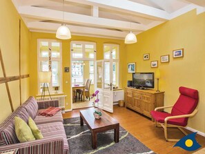 Una sala de estar con un sofá, un sillón rojo, una mesa de centro, un televisor y un comedor con mesa y sillas.