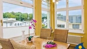 A dining area with a wooden table, wicker chairs, and large windows offering a view of buildings and trees.