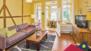 A cozy living room with a striped sofa, wooden coffee table, and a television. There are large windows and a view of the outdoors.
