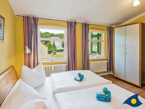 Et hotelværelse med to senge, et skab og et vindue med gardiner.