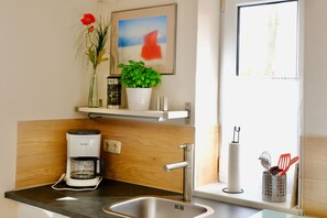 Een moderne keuken met een koffiezetapparaat, een spoelbak, een raam met uitzicht en een plank met een plant en een ingelijst foto.