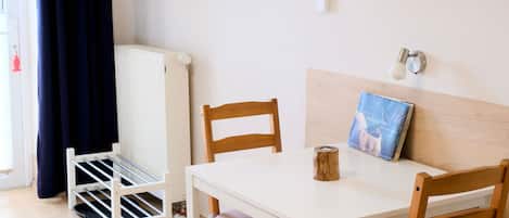 A room with a white table, two wooden chairs, a radiator, a drying rack, and a painting on the wall.