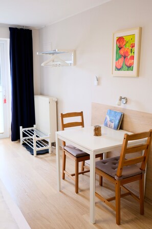 A room with a white table, two wooden chairs, a radiator, a drying rack, and a painting on the wall. - Poppy - Kunsthof Salsitz (Lohme auf Rügen)