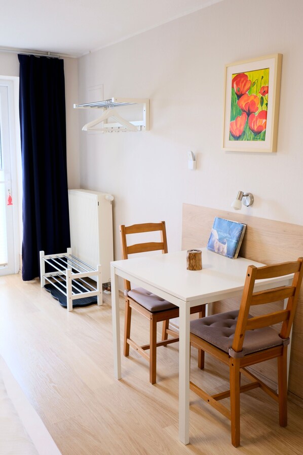 A room with a white table, two wooden chairs, a radiator, a drying rack, and a painting on the wall.