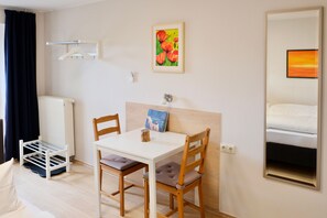 Een hotelkamer met een bed, een tafel met stoelen, een radiator, een kapstok, een schilderij en een spiegel.
