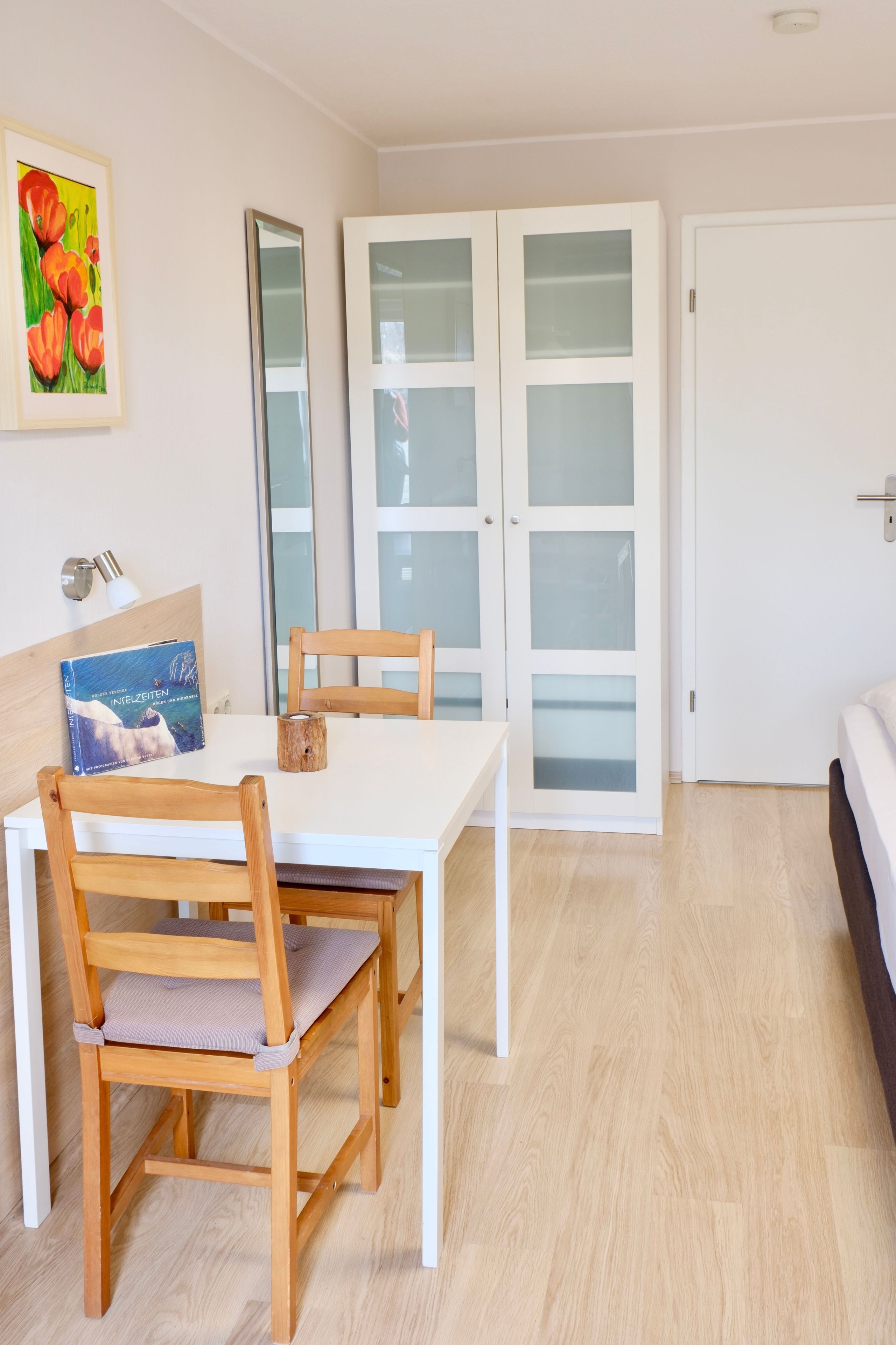 Ein Zimmer mit einem Bett, einem Tisch mit Stühlen, einer Tür mit satinierten Glasscheiben und einem gerahmten Bild an der Wand.