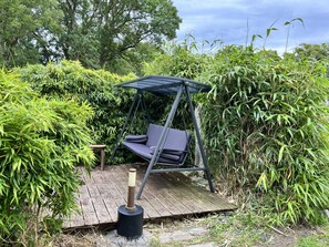 A garden with a swing chair, wooden deck, and dense foliage.