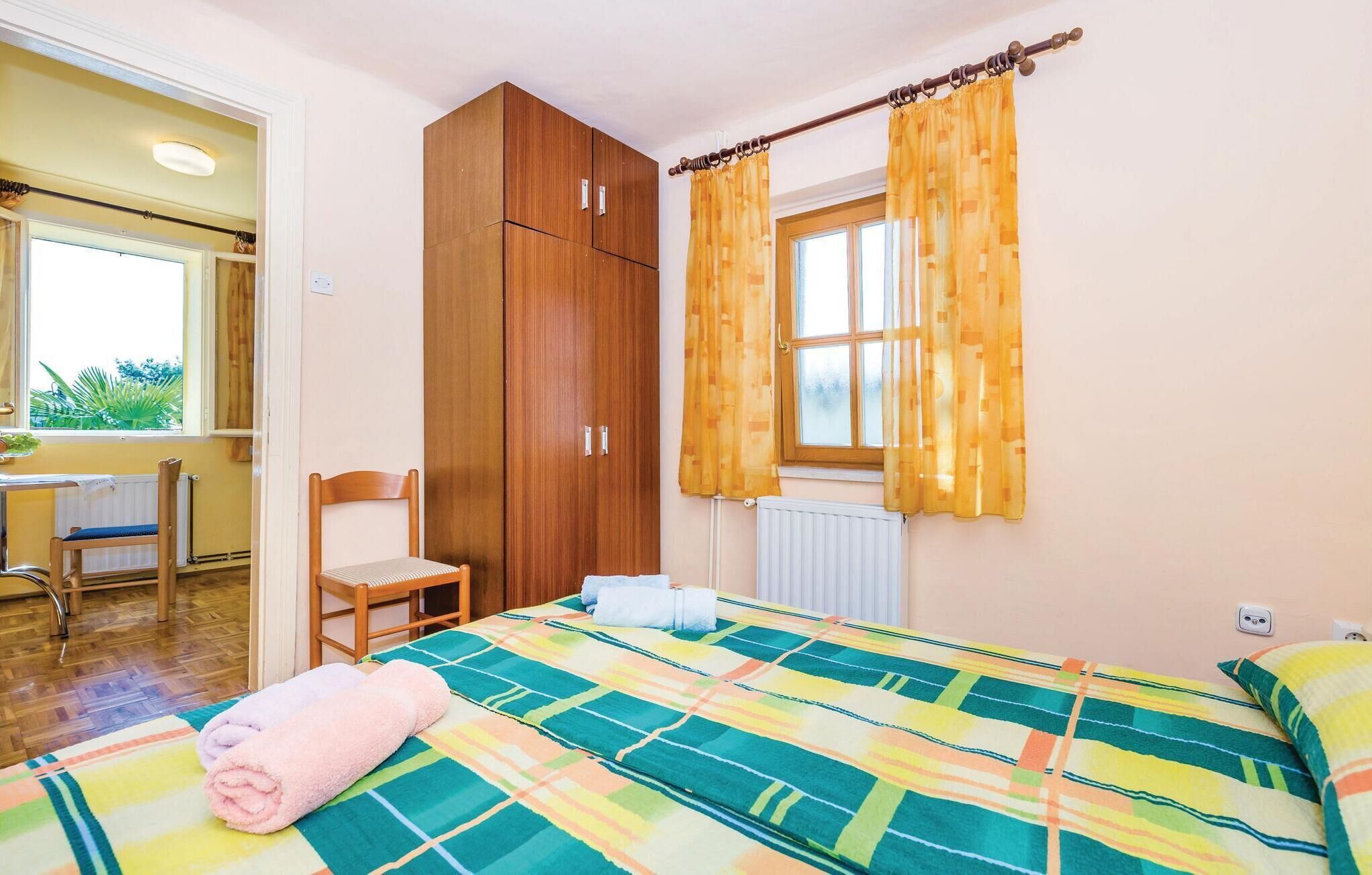 Una camera da letto con un letto, un'armadio in legno, una sedia, una finestra con tende e vista sull'esterno.