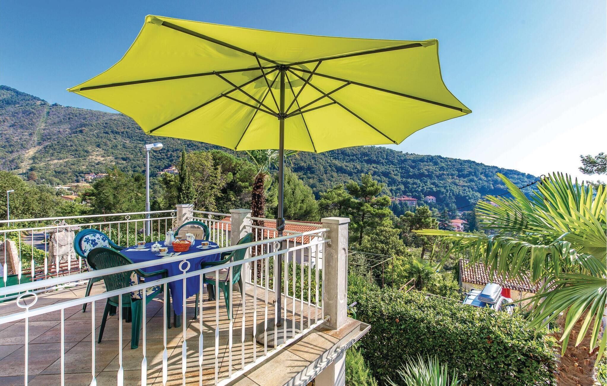Una terraza con sombrilla amarilla, mobiliario exterior y vistas panorámicas a la montaña.