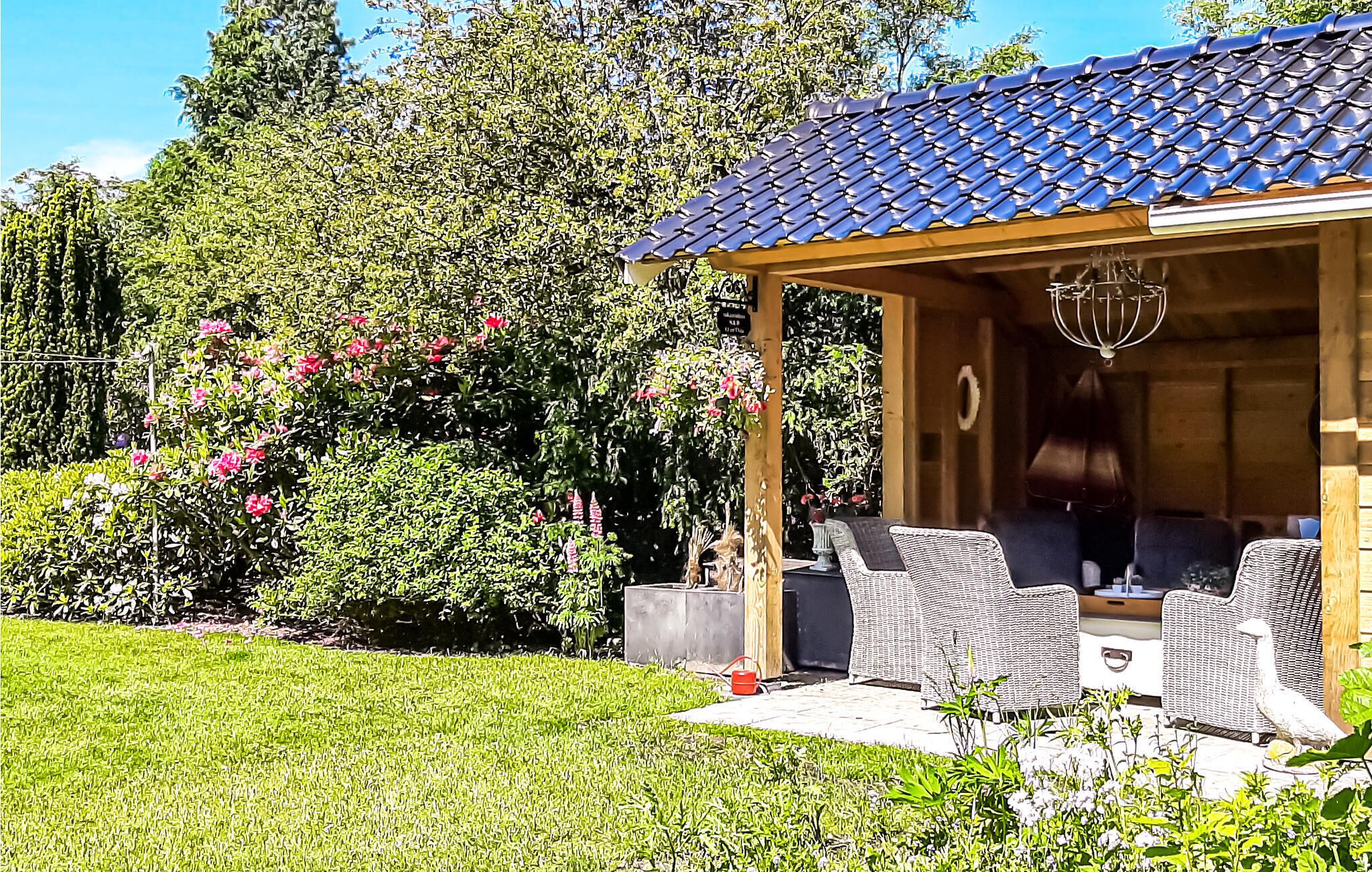 Un'area salotto esterna coperta con mobili in vimini, una pergola con tetto in tegole e un giardino con diverse piante e fiori.