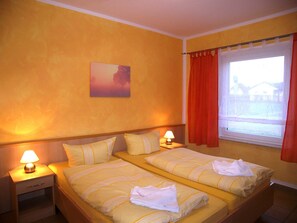 A double room with two beds, a nightstand with a lamp, a painting on the wall, and a window with curtains.