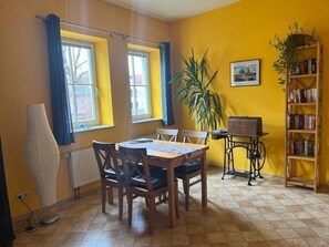 Un comedor con una mesa y sillas, un radiador, una estantería y una ventana con cortinas.