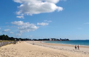 Uma extensa praia de areia dourada, com céu azul límpido e algumas nuvens esparsas.