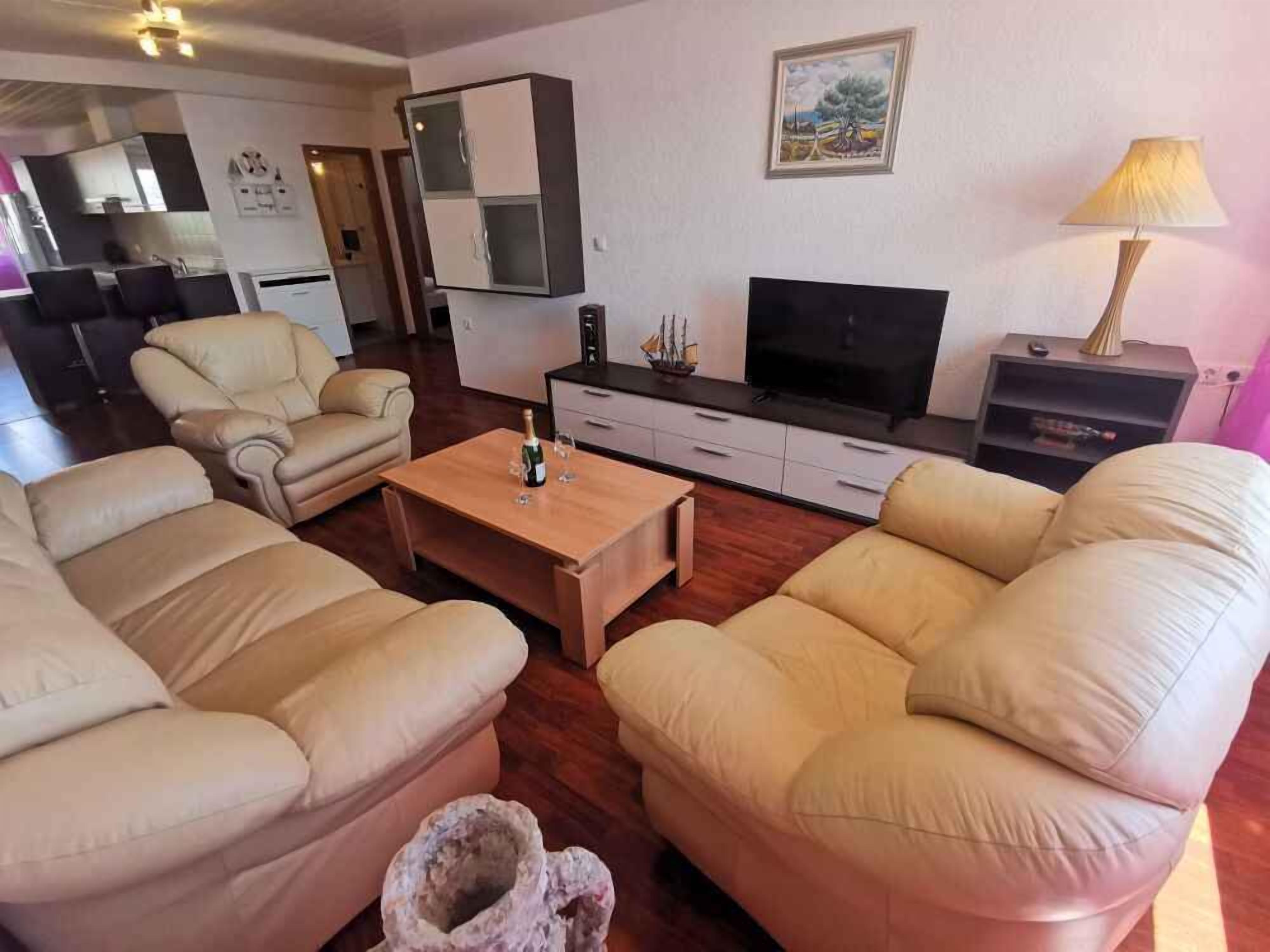 A living room with beige sofas, a wooden coffee table, a flat-screen TV, a lamp, and a painting on the wall.