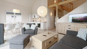 A spacious living area with a high ceiling, a staircase leading to an upper level, a dining area with white chairs, and a kitchen with modern appliances. - Amazing home in OstseeResort Olpenitz with sauna (OstseeResort Olpenitz)