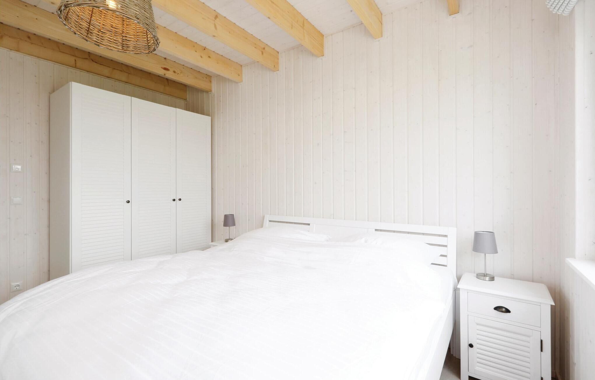 A bedroom with a large bed, wooden beams, a white wardrobe, and a bedside table with a lamp.