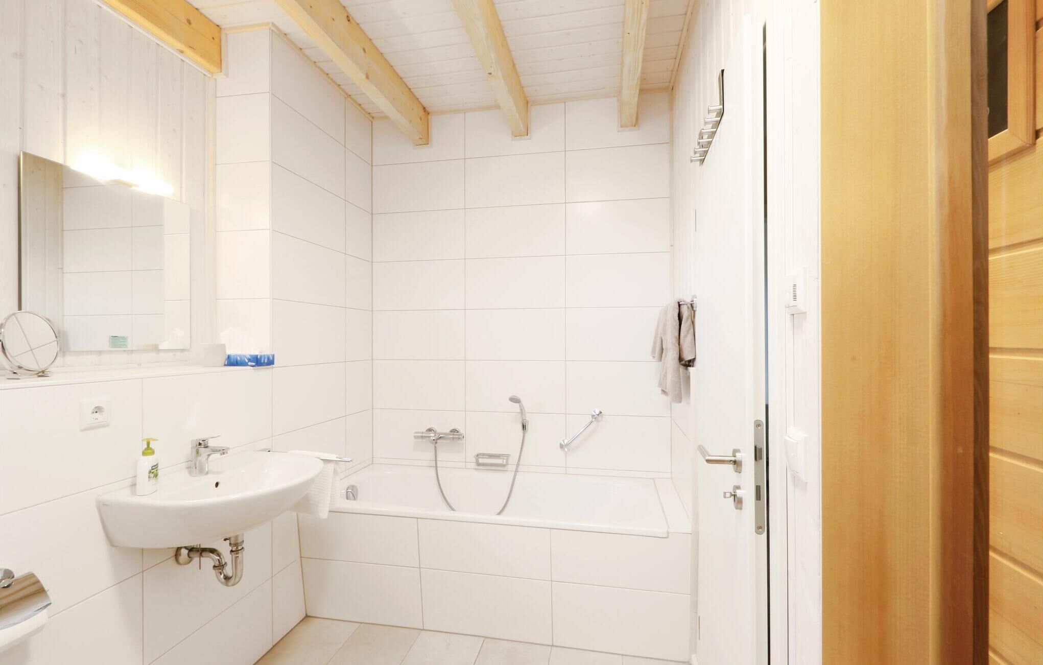 A bathroom with white tiles, a sink, a bathtub, and a shower.