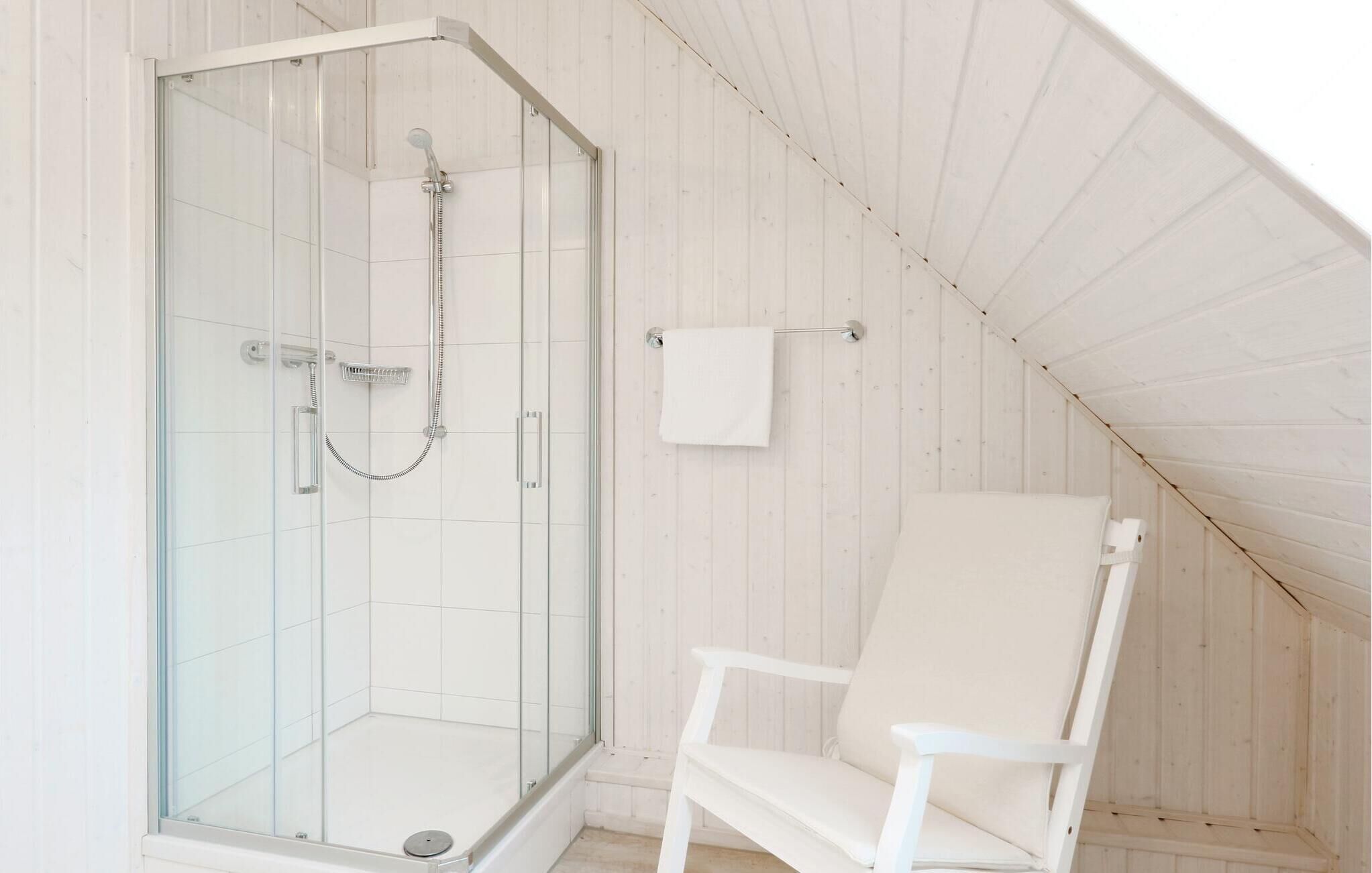 A glass-enclosed shower with a white towel rack and a white chair in a room with wooden paneling.