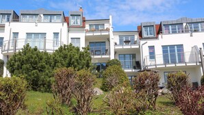 A modern multi-story residential building with balconies, large windows, and a well-maintained garden.