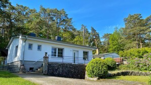 A white two-story house with a stone wall entrance, surrounded by a paved driveway and lush greenery. - Staphel - Ferienhaus Hete - dog-friendly, near the Baltic Sea - FH Hete (Sassnitz)