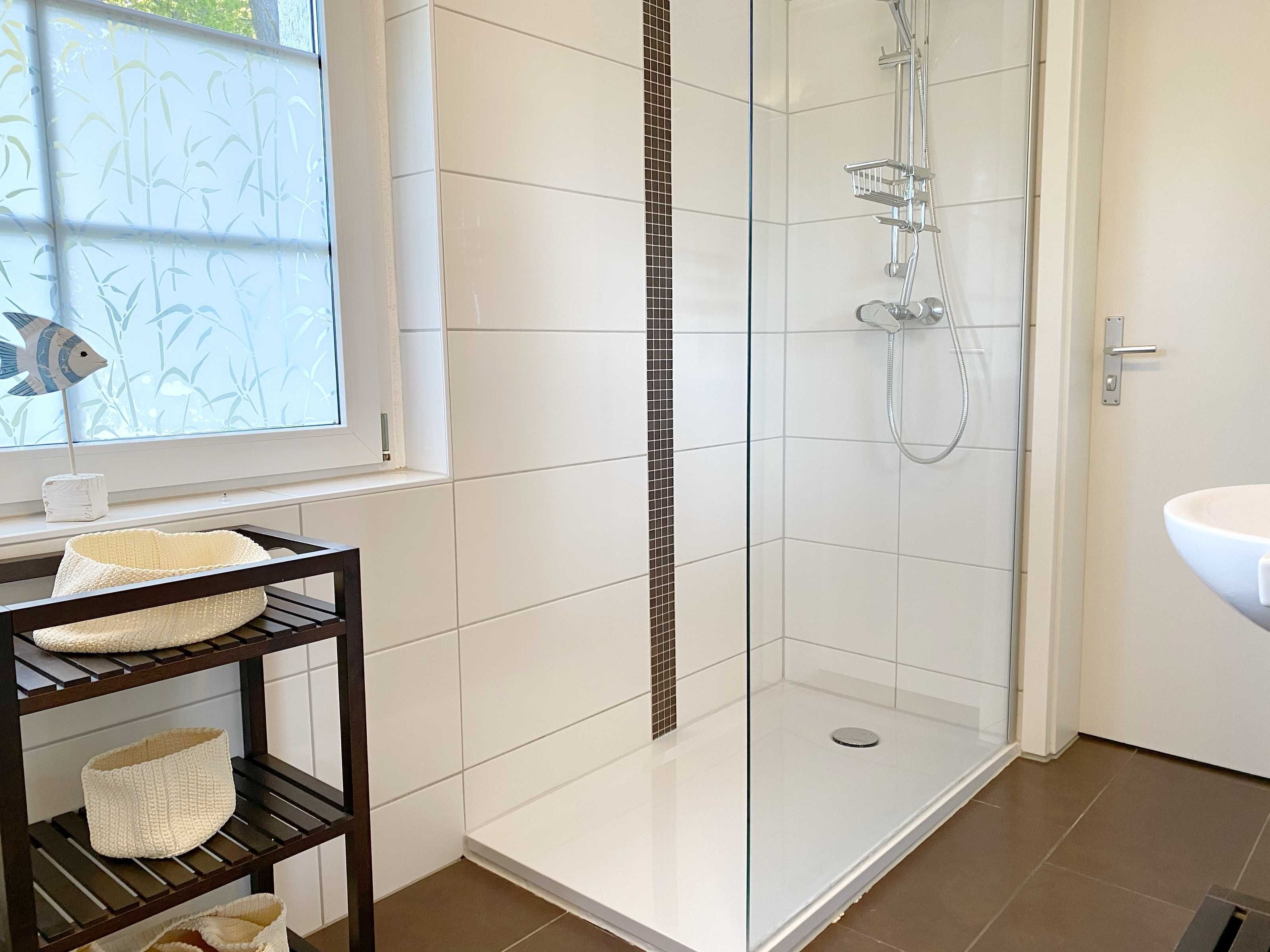 A modern bathroom with a glass-enclosed shower, white tiled walls, and a window with a decorative fish pattern.