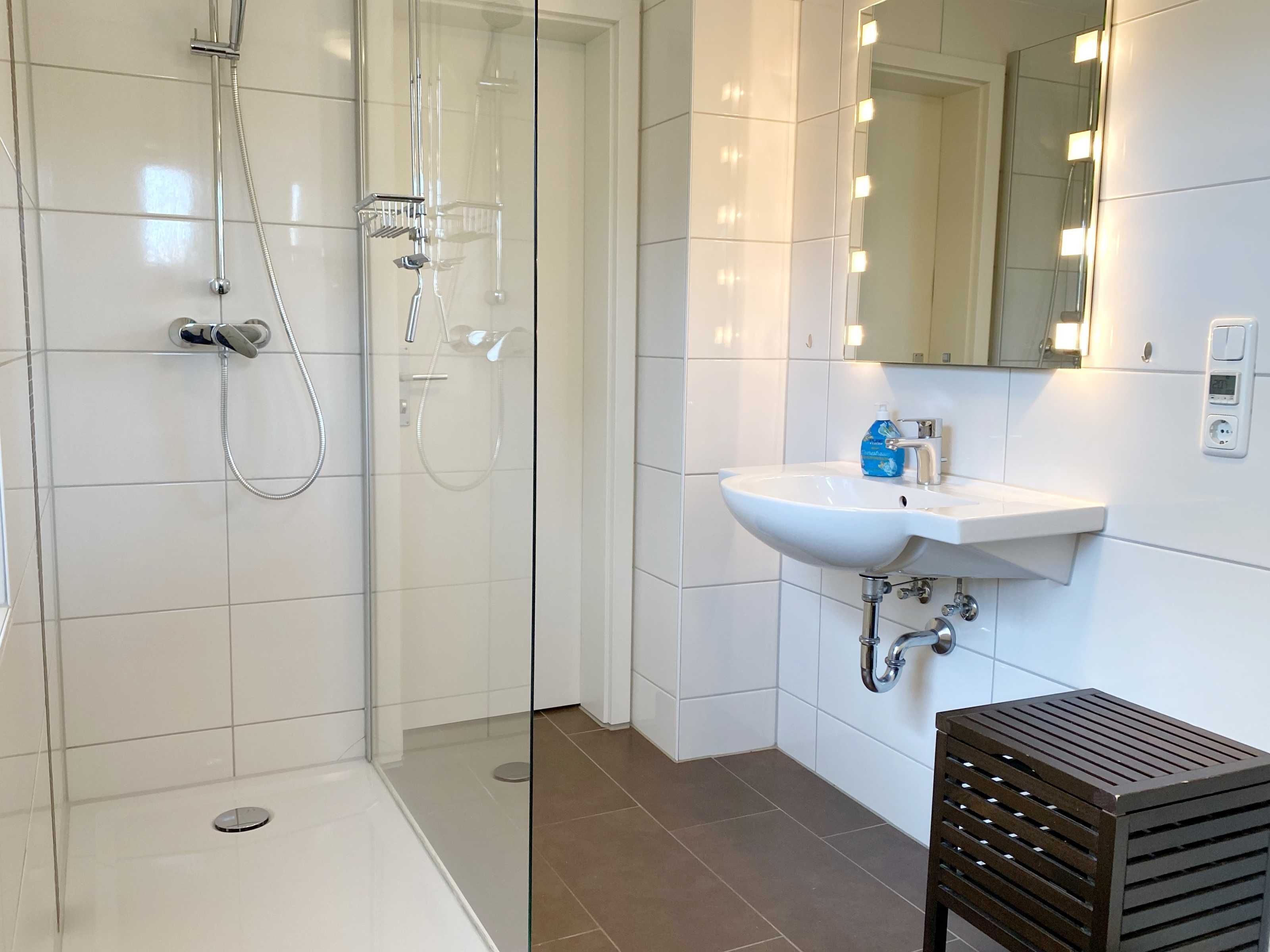 Une salle de bain moderne avec une douche à parois de verre, un lavabo blanc et un miroir avec éclairage intégré.