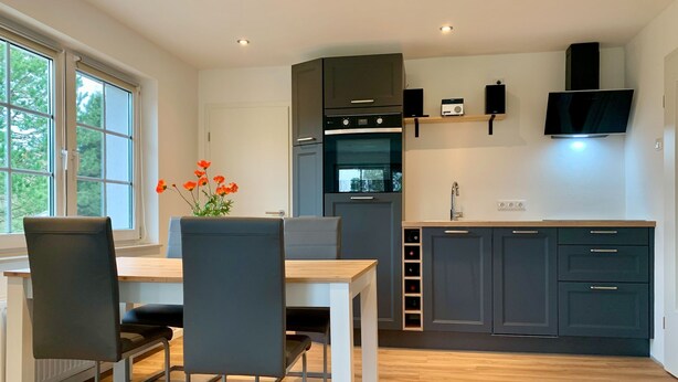 A modern kitchen with dark cabinets, a wooden countertop, and a built-in oven. There is a dining table with chairs and a vase of flowers. - Staphel - Ferienhaus Hete - dog-friendly, near the Baltic Sea - FH Hete (Sassnitz)