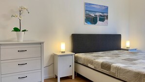 A bedroom with a bed, bedside tables with lamps, a dresser, a potted plant, and a painting on the wall. - Staphel - Ferienhaus Hete - dog-friendly, near the Baltic Sea - FH Hete (Sassnitz)