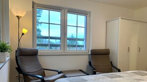 Une chambre avec deux chaises, un lit recouvert d’une courtepointe, une fenêtre et une armoire.