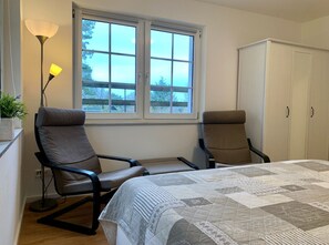 Een slaapkamer met twee stoelen, een bed met quilt, een raam en een kledingkast.