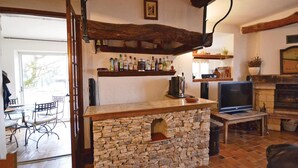 Una cocina rústica con un arco de piedra, estantes de madera con botellas, un televisor y una chimenea.