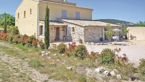 Una casa de dos pisos con fachada de piedra, techo de tejas y un pequeño patio con mobiliario exterior.