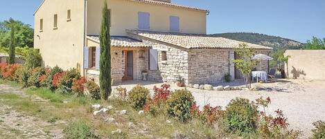A two-story house with a stone facade, a tiled roof, and a small patio area with outdoor furniture.