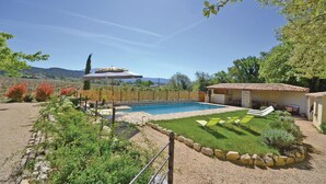 Un área de piscina con terraza de piedra, rodeada de césped cuidado y diversas plantas.