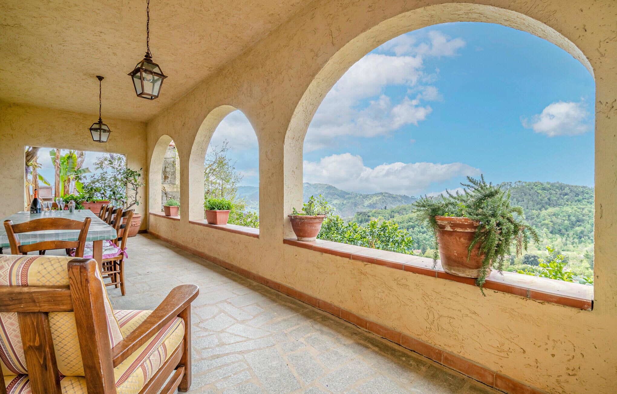 Un comedor con una mesa dispuesta para cuatro personas, rodeado de ventanales arqueados con vistas a un paisaje montañoso.