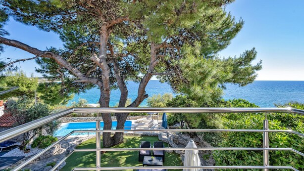 Un balcón con vistas al mar, una piscina y mobiliario exterior.
