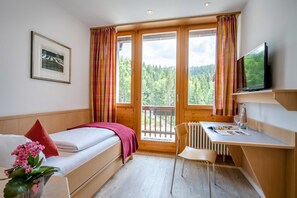 Una habitación con cama, escritorio, silla, televisión y ventana con cortinas.