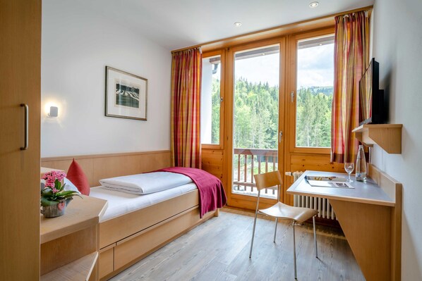 Een kleine kamer met een bed, bureau, stoel en een raam met gordijnen.