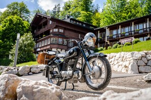 Una motocicleta antigua estacionada frente a un edificio grande de varios pisos, con un letrero que indica que es un 'Berghotel'.