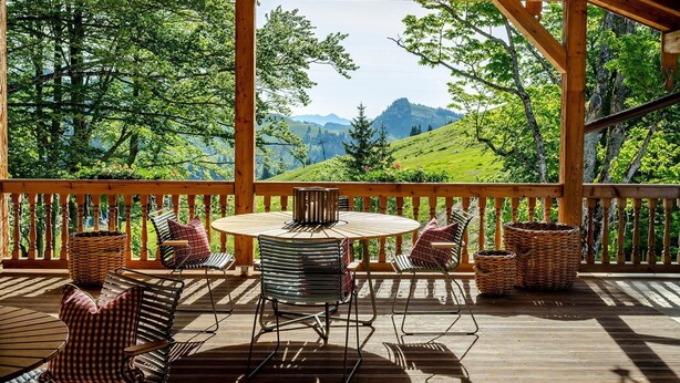 A wooden deck with a round table and chairs, overlooking a mountainous landscape. - Single room - Berghotel Sudelfeld (Bayrischzell)